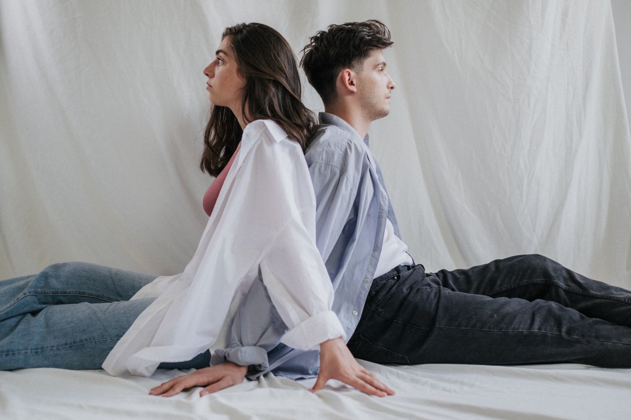 Pareja joven sentada espalda con espalda, mirando en direcciones opuestas, que ilustra la diferencia de deseo en la pareja.